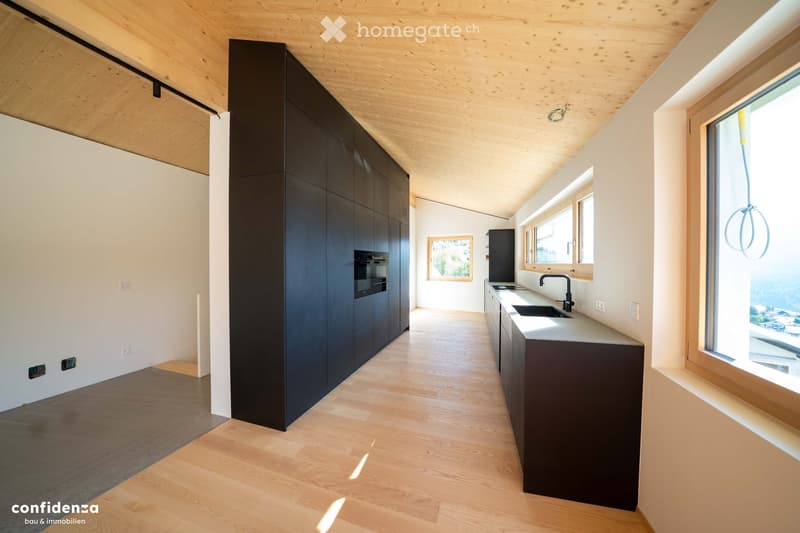 Modern kitchen with dark cabinets, light wooden flooring, and large windows offering a scenic view.