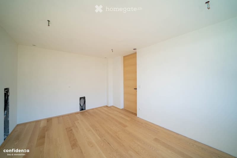 Empty room with light-colored walls and wooden flooring, featuring a single wooden door and minimal fixtures.
