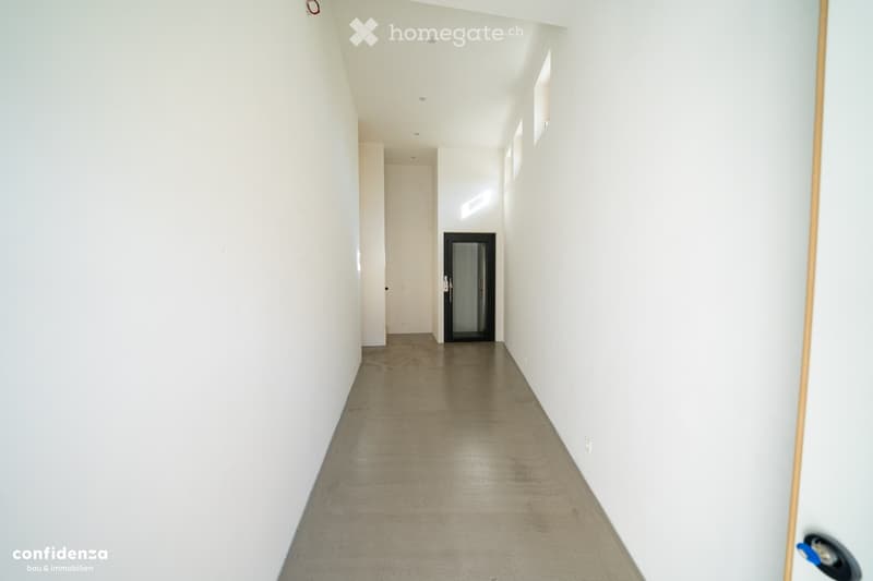 Empty hallway with white walls, concrete floor, and a single door at the end.