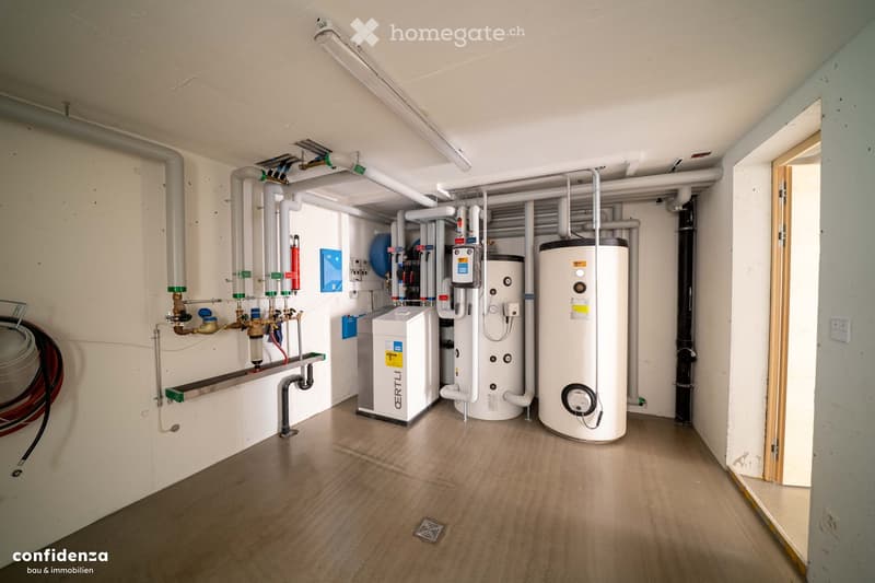 Utility room with water heaters, pipes, valves, and control panels mounted on the walls.