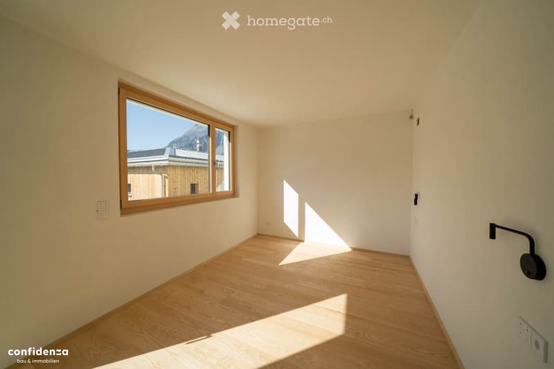 Empty room with light wooden flooring, white walls, and a large window with wooden frame letting in natural light. No furniture or equipment present.