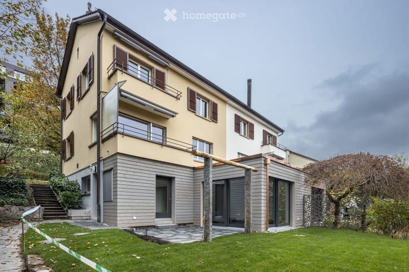 Two-story house with beige facade, multiple windows, balconies, and a modern extension with large glass doors.