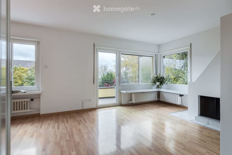 Empty room with wooden flooring, large windows, radiators, and a fireplace. No furniture or equipment present.
