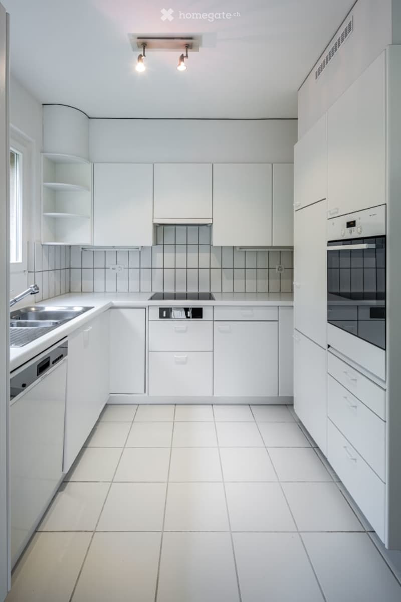 Modern, minimalist kitchen with white cabinets, a stainless steel sink, and built-in appliances including an oven and dishwasher.