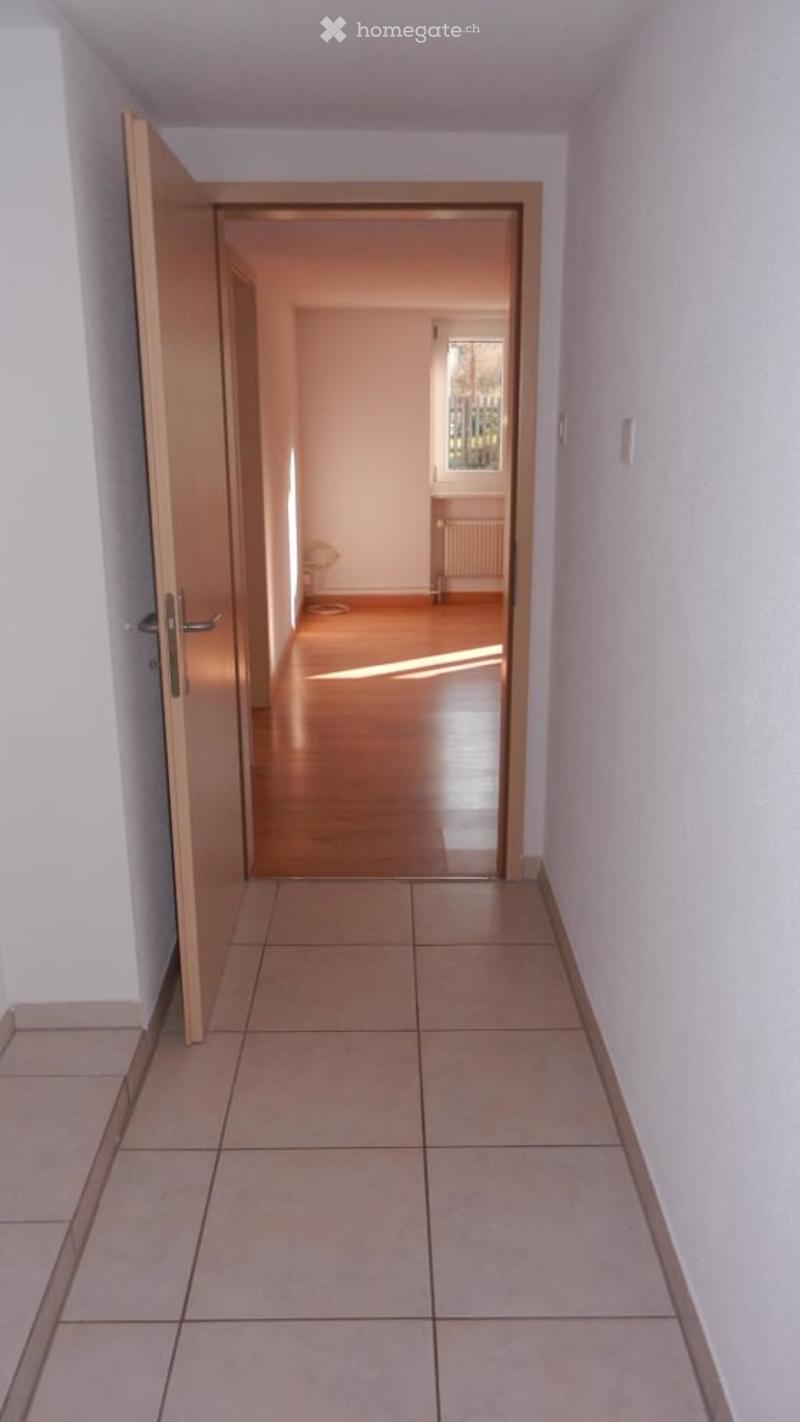 Empty hallway with white walls, wooden floor, open door, window with white radiator