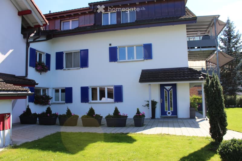2 story house, white exterior, blue shutters, blue door, balcony, well-maintained garden, multiple potted plants