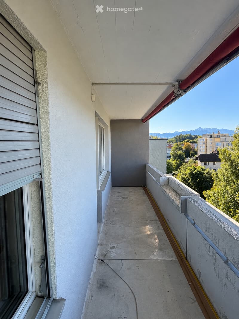 Balcony with concrete floor, white walls, and a view of trees and mountains in the background.