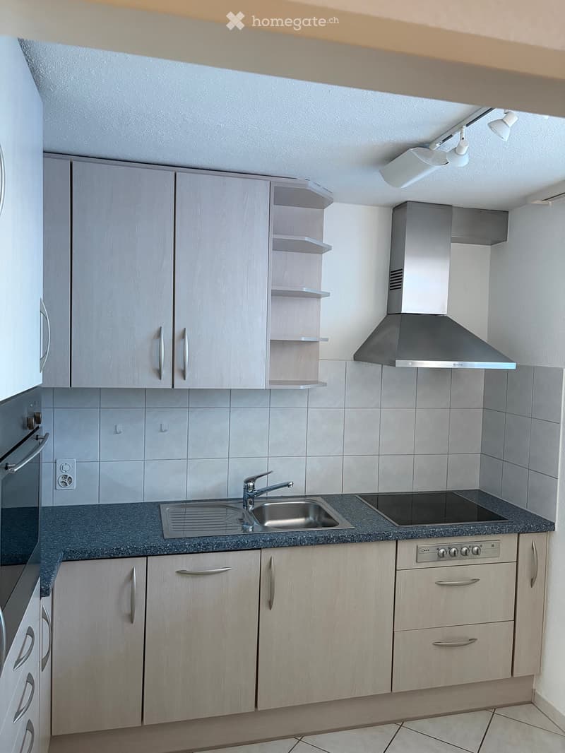 Modern kitchen with light wood cabinets, stainless steel appliances, granite countertop, and built-in lighting.
