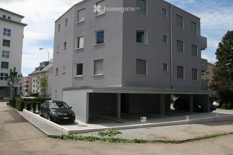 Modern multi-story building with a garage and several parked cars in front.