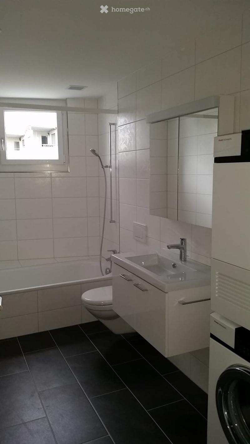 Modern bathroom with white tiles, black floor, bathtub, toilet, sink, mirror, and shower.