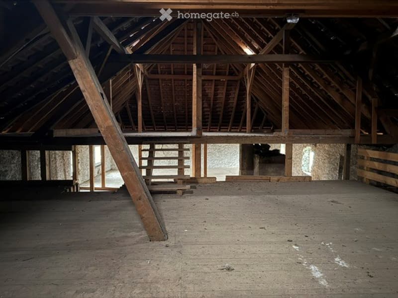 Empty attic space with wooden beams, exposed rafters, and a concrete floor. No furniture or equipment present.