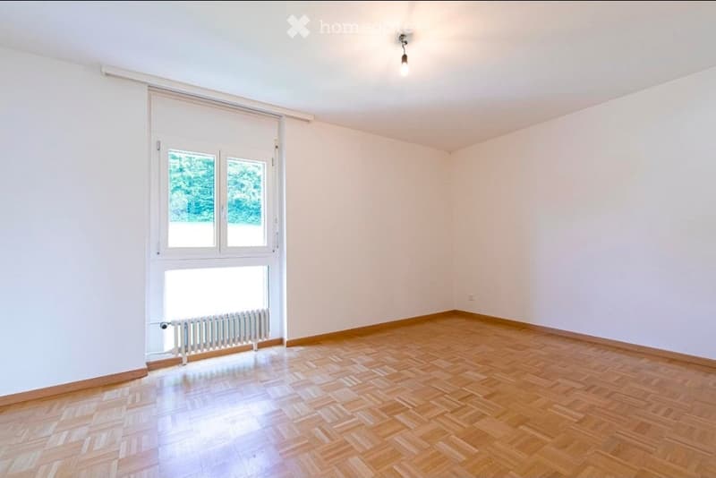 Empty room with wooden flooring, white walls, large windows, and a radiator under the window.