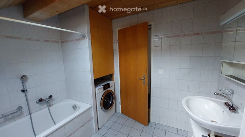 Bathroom with a bathtub, sink, washing machine, wooden cabinet, and shelves.