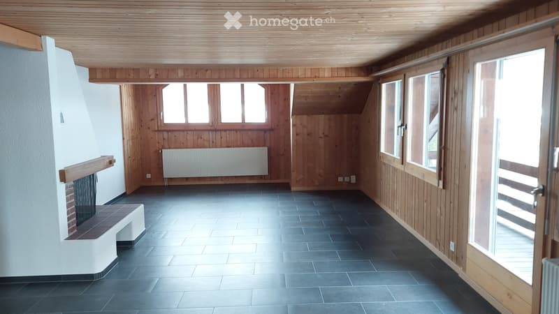 Empty room with wooden walls, dark tiled floor, large windows, and a fireplace area.