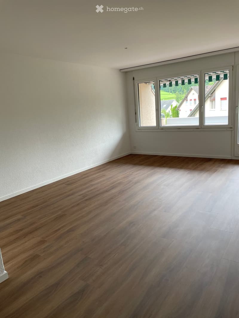 Empty room with wooden flooring and large windows offering a view of the outside area.