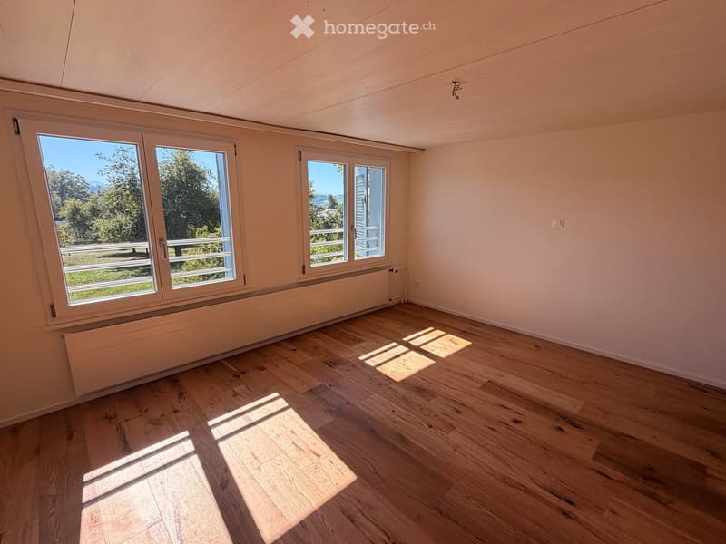 Empty room with wooden flooring, large windows, and radiators. Natural light streams in, casting shadows on the floor.