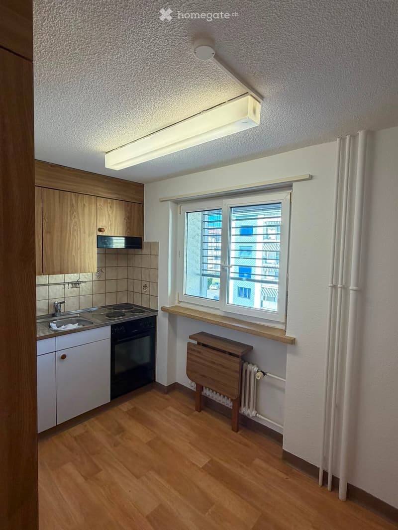 Compact kitchen with wooden cabinets, a sink, stove, and a small table near the window.