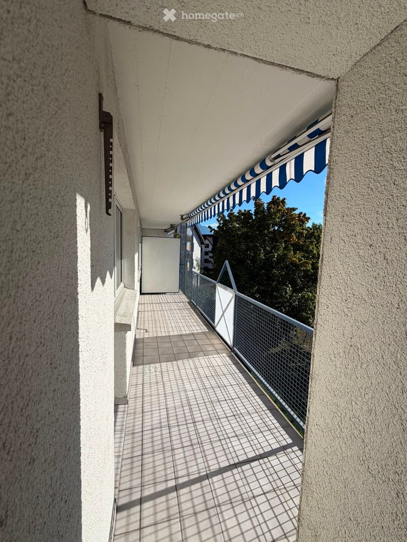 Balcony with tiled floor, metal railing, and striped awning, leading to a door.
