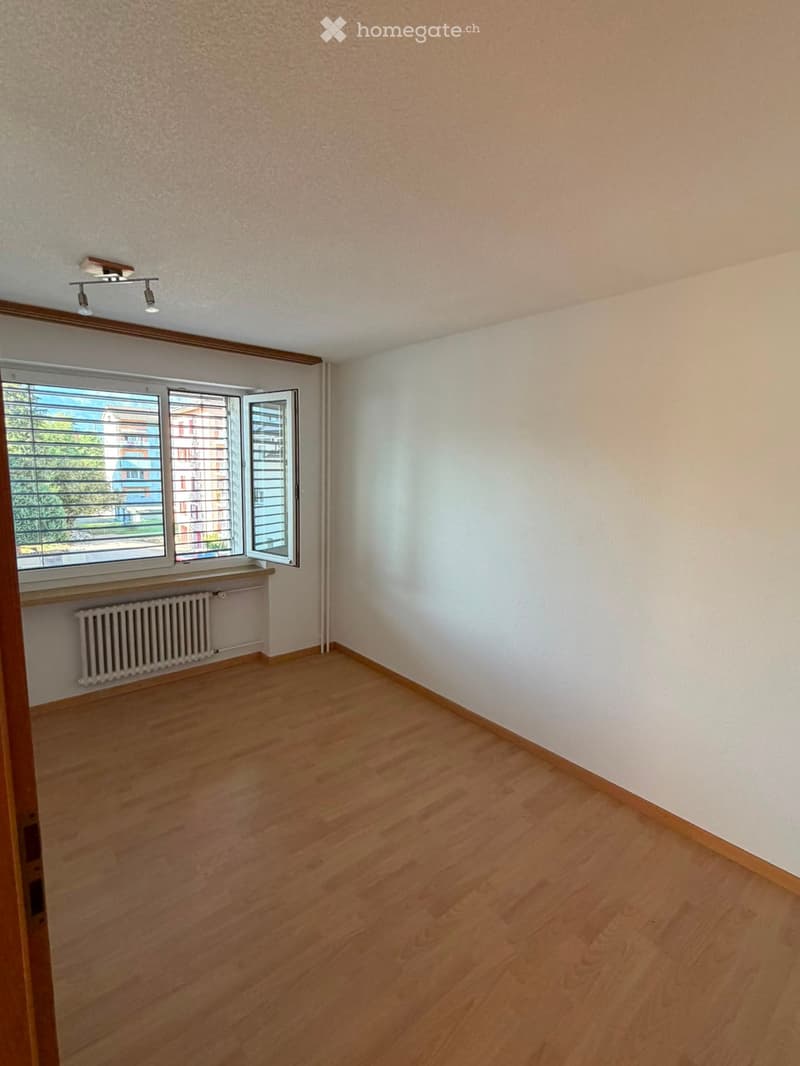 Empty room with wooden flooring, white walls, a window with blinds, and a radiator below the window.