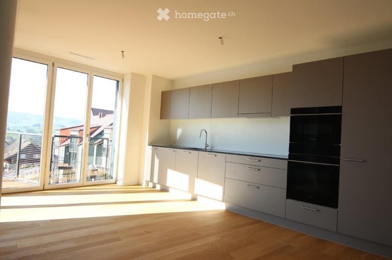 Modern kitchen with grey cabinets, white countertops, wooden flooring, and large windows offering a scenic view.