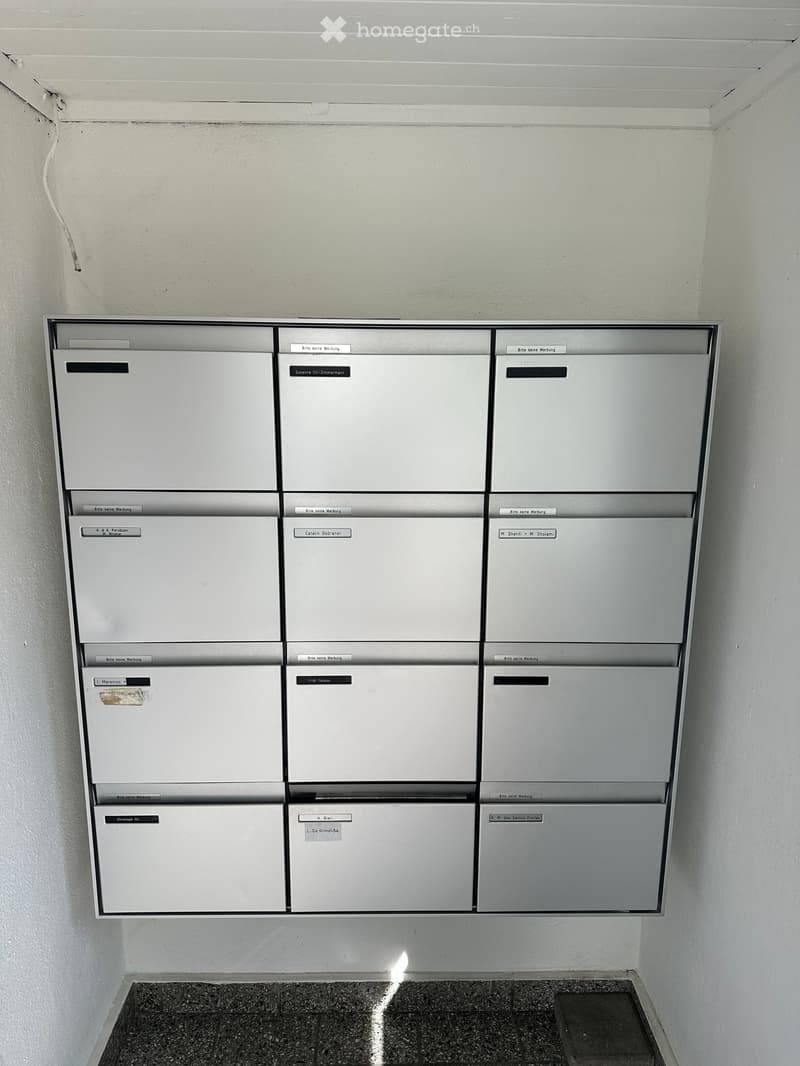 A row of white mailboxes mounted on a wall in a hallway, each labeled with names and instructions in German.
