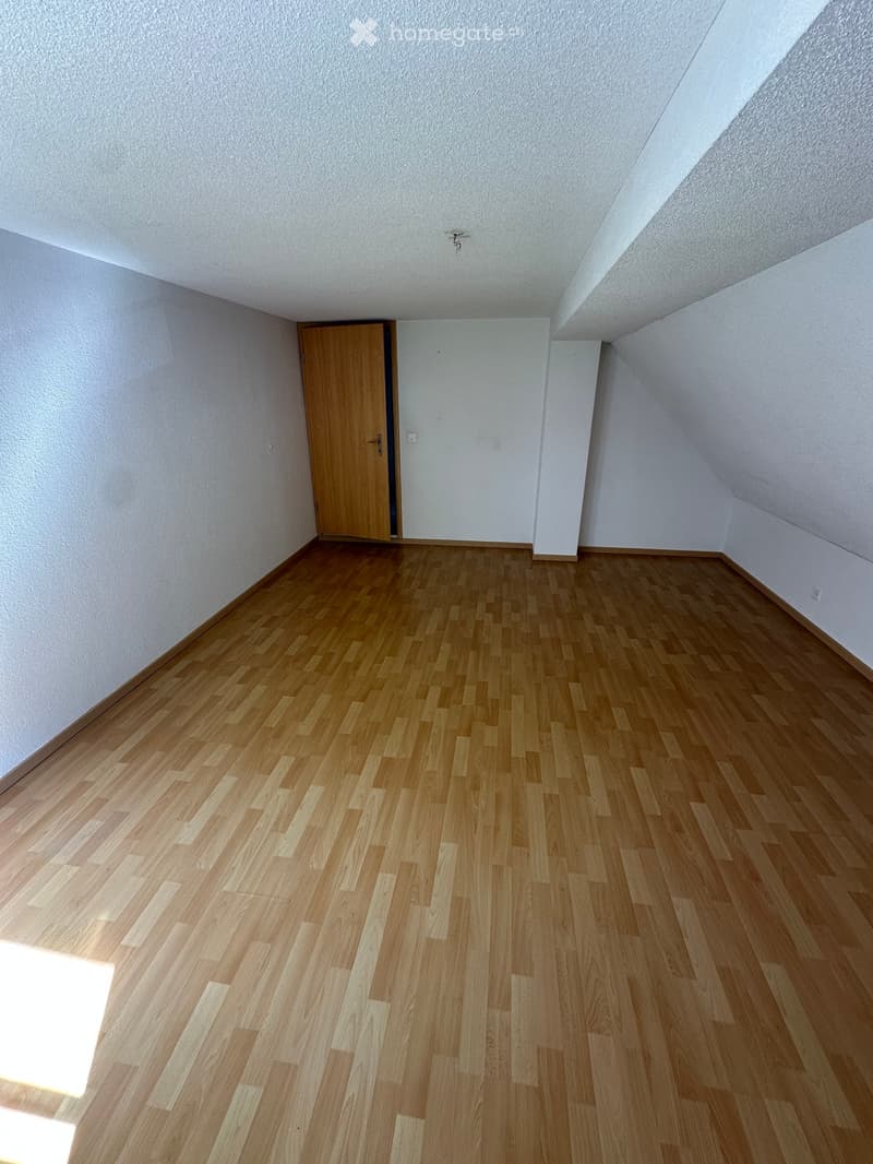 Empty room with wooden flooring, white walls, and a single wooden door.