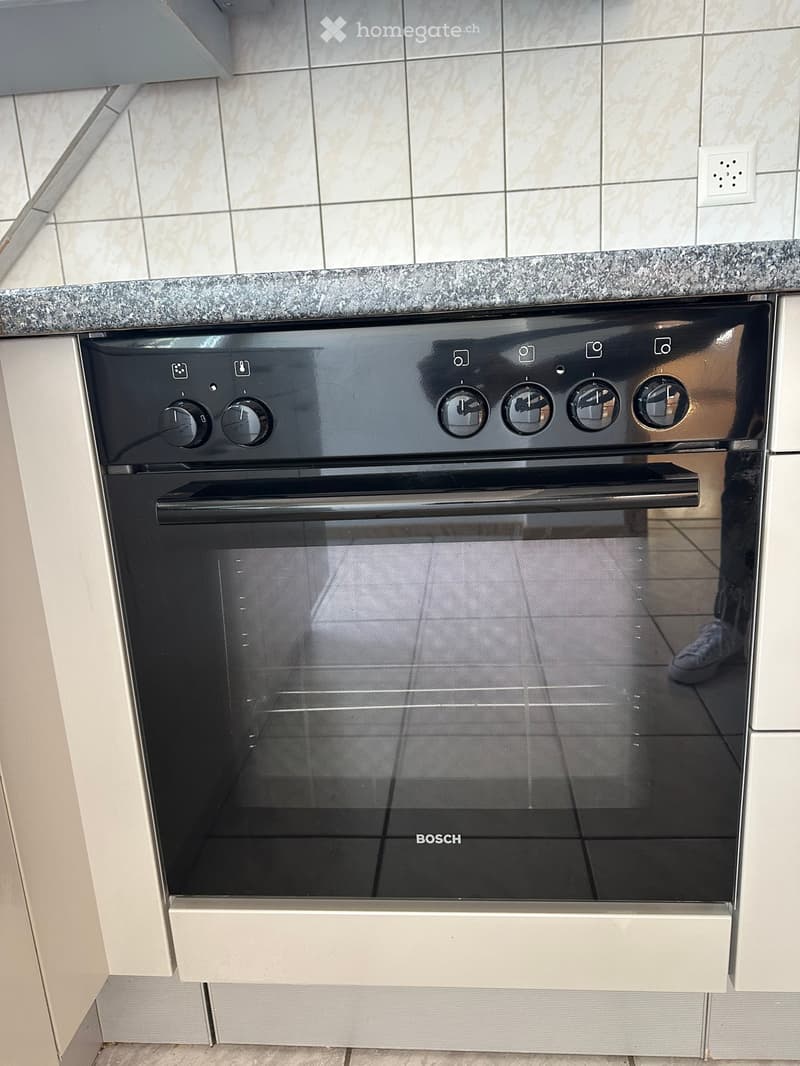 Modern black Bosch oven with multiple control knobs and a glass door, integrated into a kitchen with a granite countertop and tiled walls.