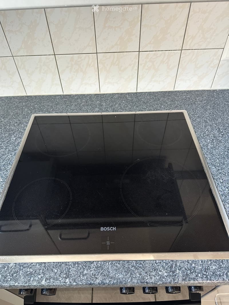 Modern kitchen with a Bosch induction cooktop featuring four cooking zones, placed on a granite countertop with beige tiled walls.
