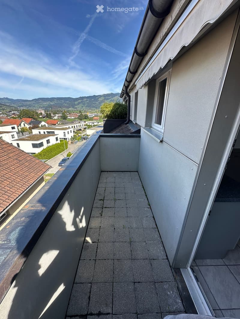 Balcony with tiled floor, metal railing, and a view of a suburban neighborhood with houses and mountains in the background.