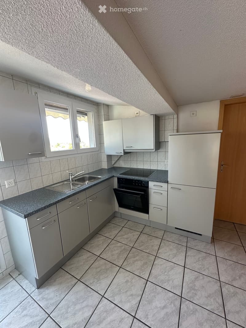 Modern kitchen with grey cabinets, a sink, an oven, and a refrigerator. The space features tiled walls and a tiled floor, with a window providing natural light.