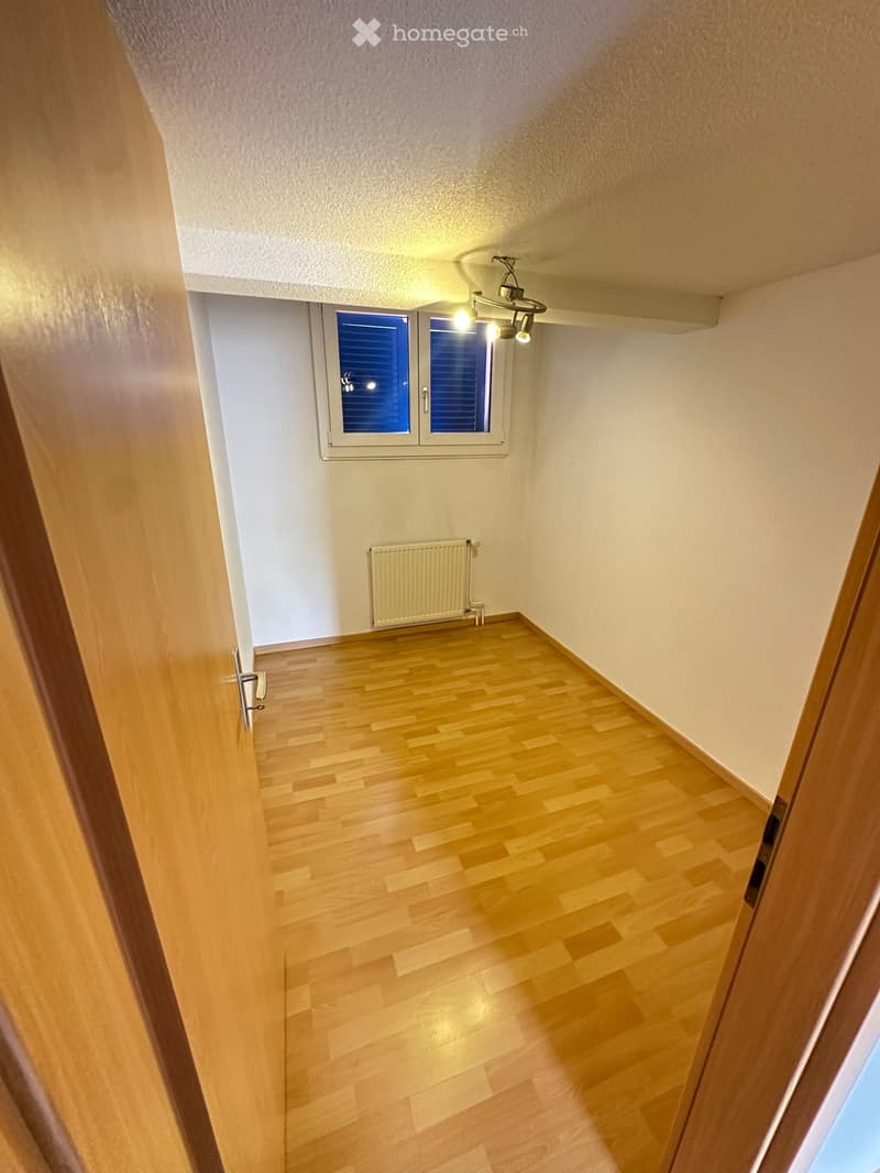 Empty hallway with wooden flooring, white walls, a window with blinds, and a radiator. No furniture or equipment present.