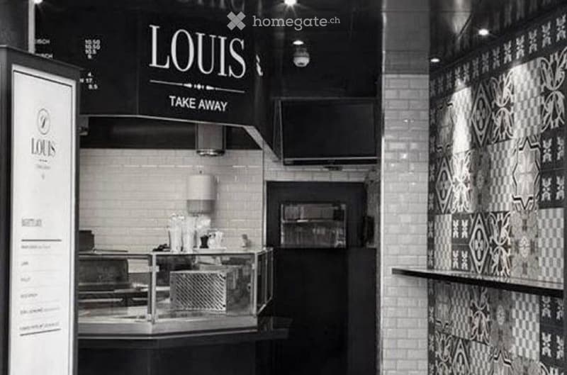 Modern take-away restaurant interior with a counter, lamp, menu board, and screen. The walls are decorated with patterned tiles, and the space is well-lit with recessed lighting.