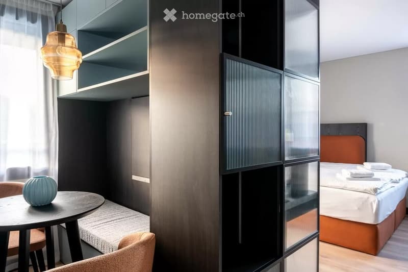 Modern, compact bedroom with a built-in bed, round table, chairs, decorative vase, and shelves.