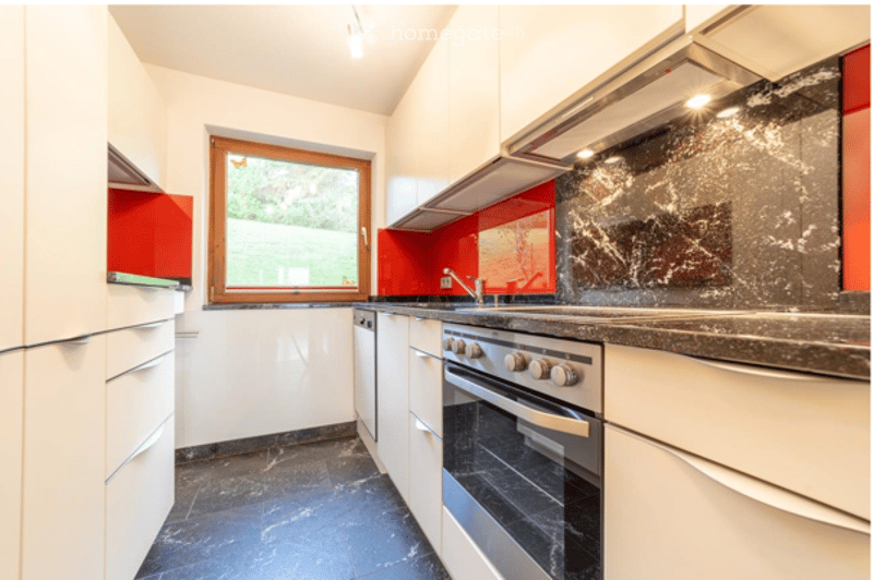 Modern kitchen with white cabinets, stainless steel appliances, a black marble backsplash, and a red accent wall.