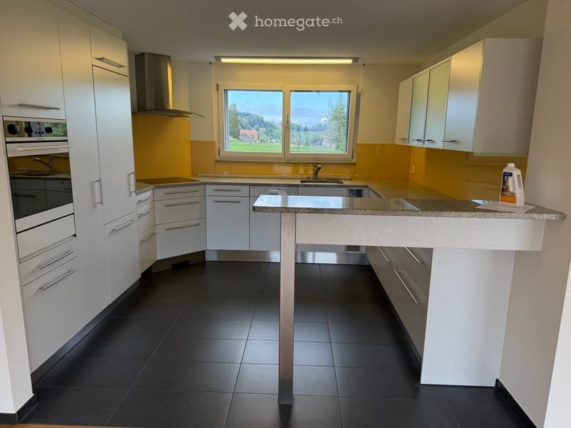 Modern kitchen with white cabinets, black tiled floor, central island, and large windows overlooking a scenic view.