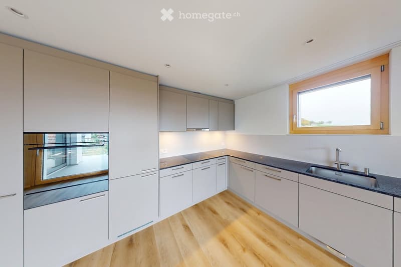 Modern kitchen with white cabinets, wooden flooring, and stainless steel appliances including an oven and sink.