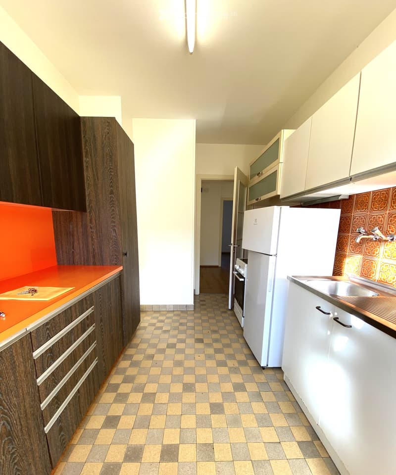 Modern kitchen with white and dark wood cabinets, a stainless steel sink, and a refrigerator. The floor is tiled, and the countertops are orange.