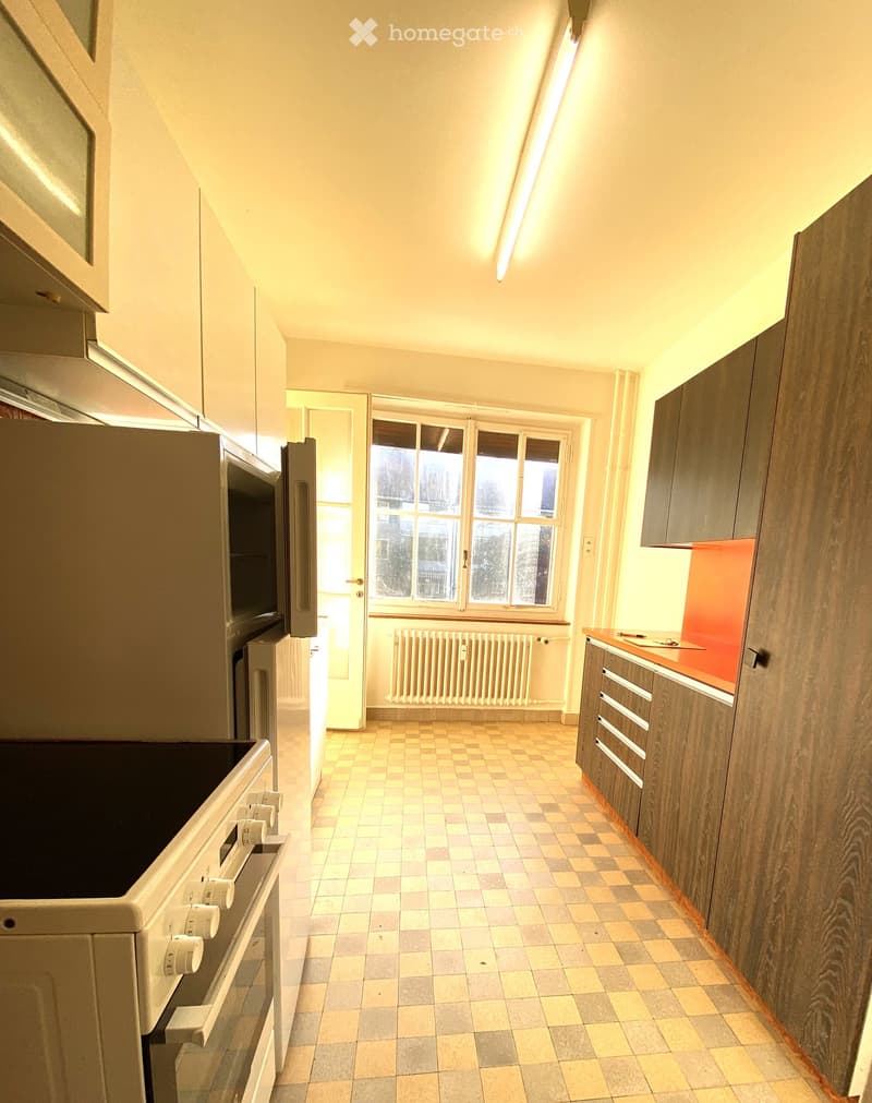 Modern kitchen with wooden cabinets, tiled floor, and large windows. Features an oven, refrigerator, and built-in cabinets.