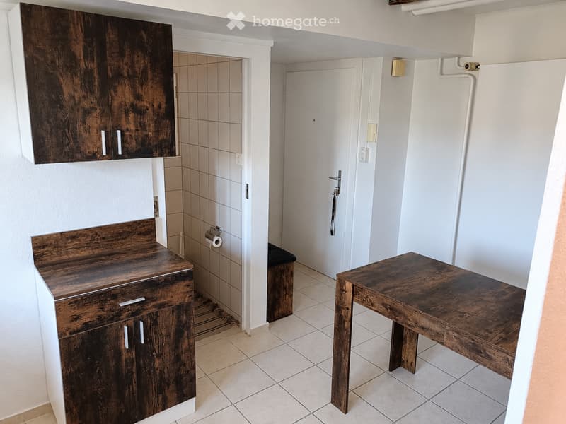 Bathroom with wooden cabinets, a small stool, and a wooden table. The space includes a toilet and a shower area with tiled walls.