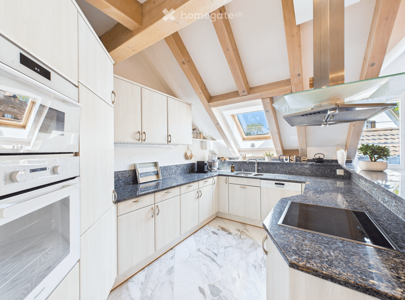 Modern kitchen with white cabinets, marble flooring, stainless steel appliances, and a skylight offering a view.