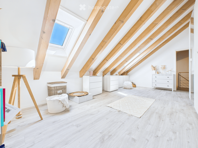 Bright, airy attic room with wooden beams and skylights. Features include a white floor lamp, wicker basket, white dresser, white cabinet, white rug, stool, and a mirror on the wall.