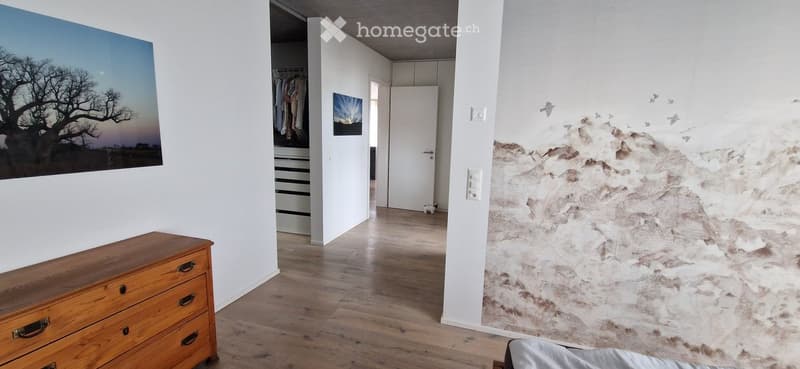 A modern hallway with wooden flooring, white walls, a dresser, a wardrobe, and artwork on the walls.
