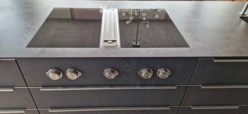 Modern kitchen with dark grey cabinets, multiple drawers with metallic knobs, and a sleek sink with a mirrored backsplash.