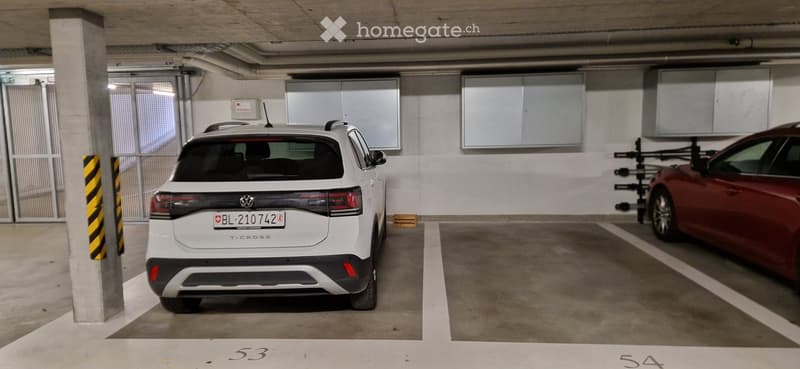 Underground parking area with two cars parked in designated spots, white Volkswagen T-Cross and red car, marked parking spaces numbered 53 and 54.
