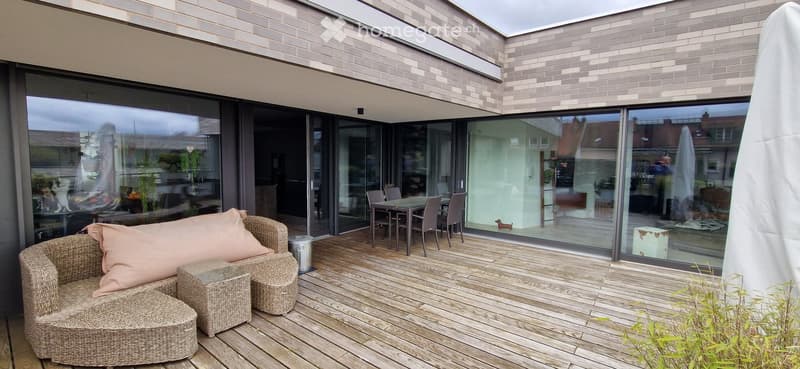 Wooden deck with wicker seating, glass sliding doors leading to interior, modern brick facade.