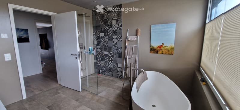 Modern bathroom with a freestanding bathtub, glass-enclosed shower, towel rack, and artwork on the wall.