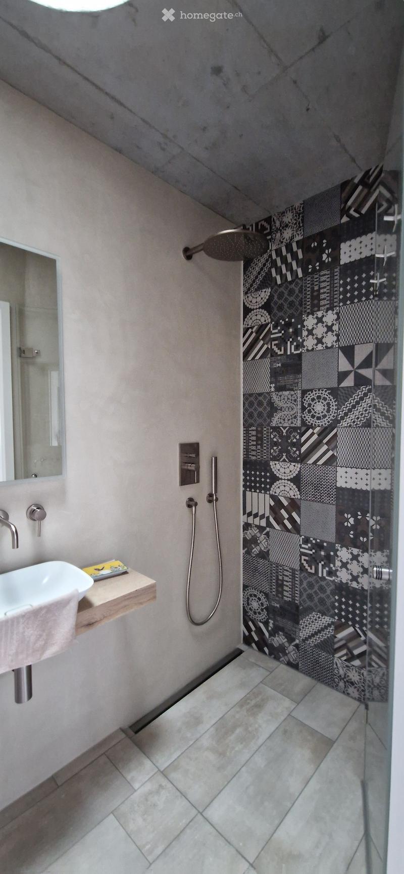 Modern bathroom with a white sink, sleek faucet, mirror, and a glass-enclosed shower with black and white patterned tiles.