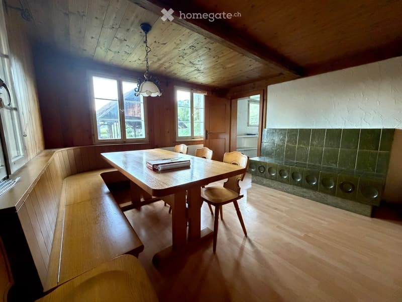 Bright, wooden-floored room with a large wooden table, chairs, built-in bench seating, and a stone fireplace with circular glass panels.