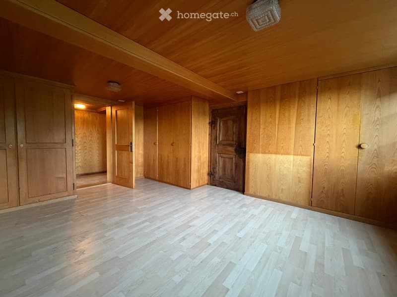 Empty room with wooden walls, wooden floor, and several doors leading to other spaces.
