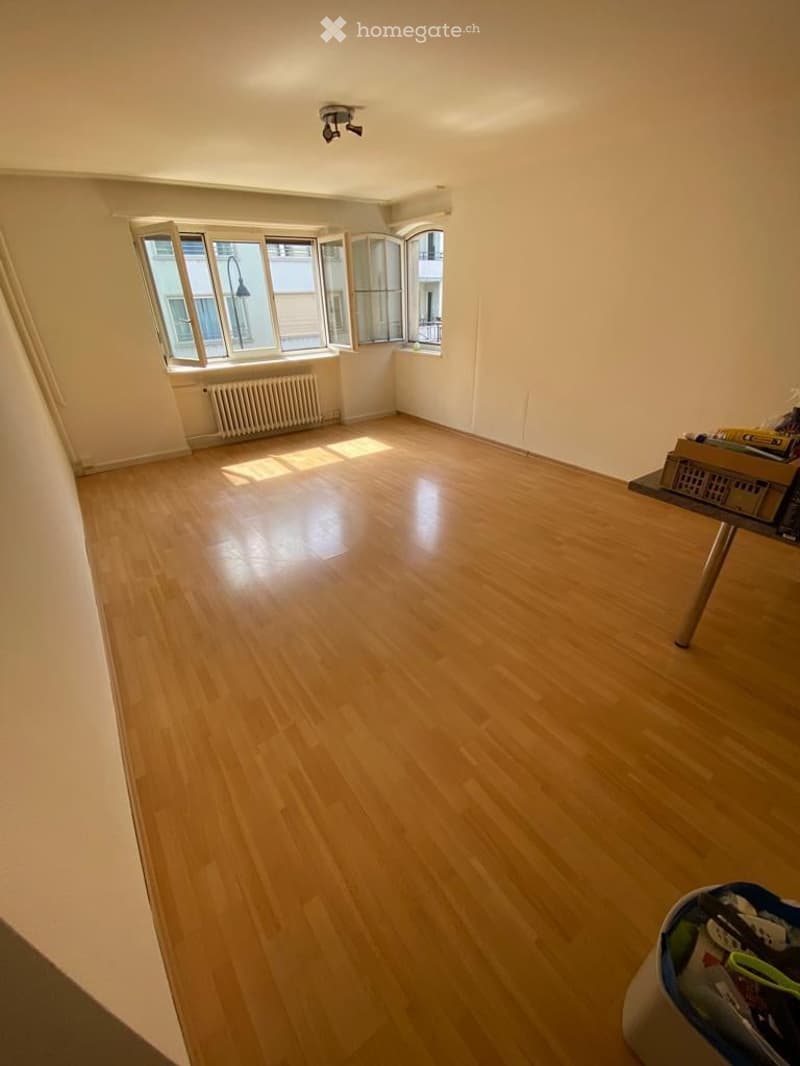 Empty room with wooden flooring, large windows, and a radiator. No furniture or equipment present.